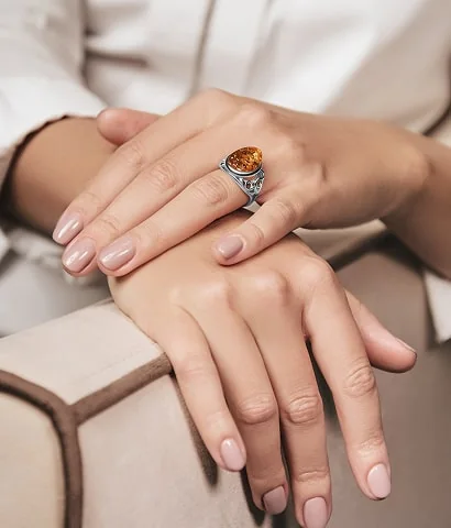 Hands wearing a silver ring with an amber stone